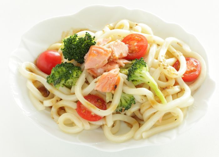 A bowl of salad udon, featuring udon with broccoli, tomatoes, and salmon flakes.